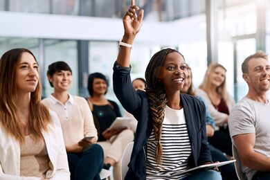 Dame die haar hand op steekt in een ruimte vol mensen